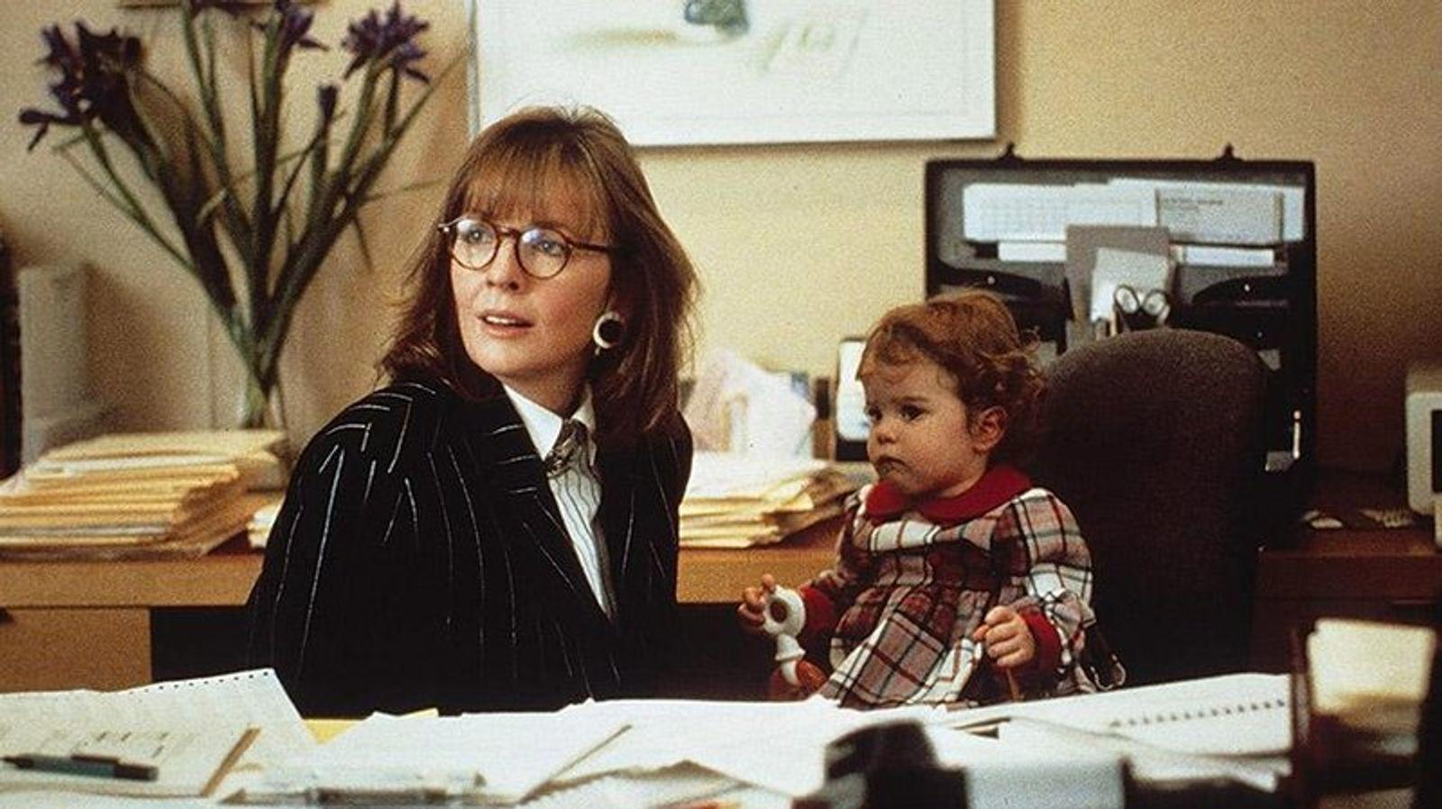 Eine Frau mit Brille und ein Baby sitzen an einem Schreibtisch.