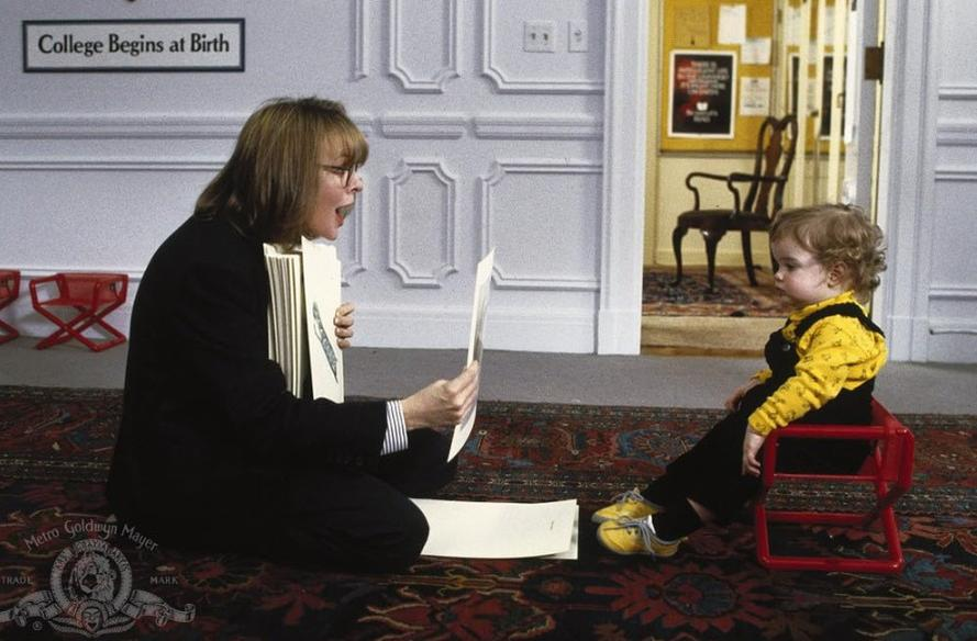 Eine Frau liest einem Kleinkind auf einem Teppich vor. Ein Schild besagt „College Begins at Birth“.