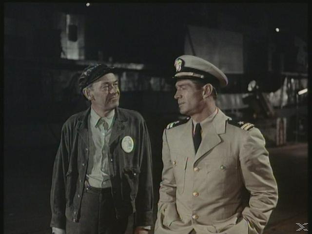 Ein Mann in Uniform und ein Arbeiter stehen nachts vor einem Schiff.