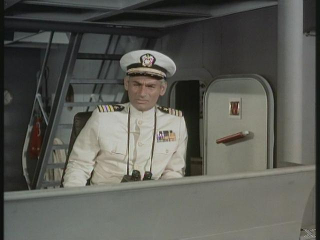 Ein Mann in weißer Uniform mit Hut und Fernglas sitzt an Deck.
