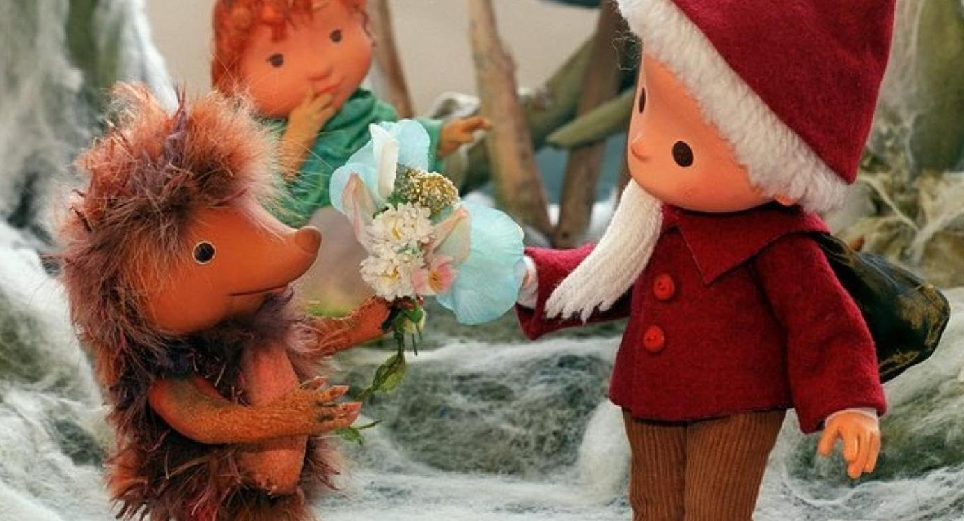 Ein Igel gibt einem Jungen mit Weihnachtsmütze einen Blumenstrauß.