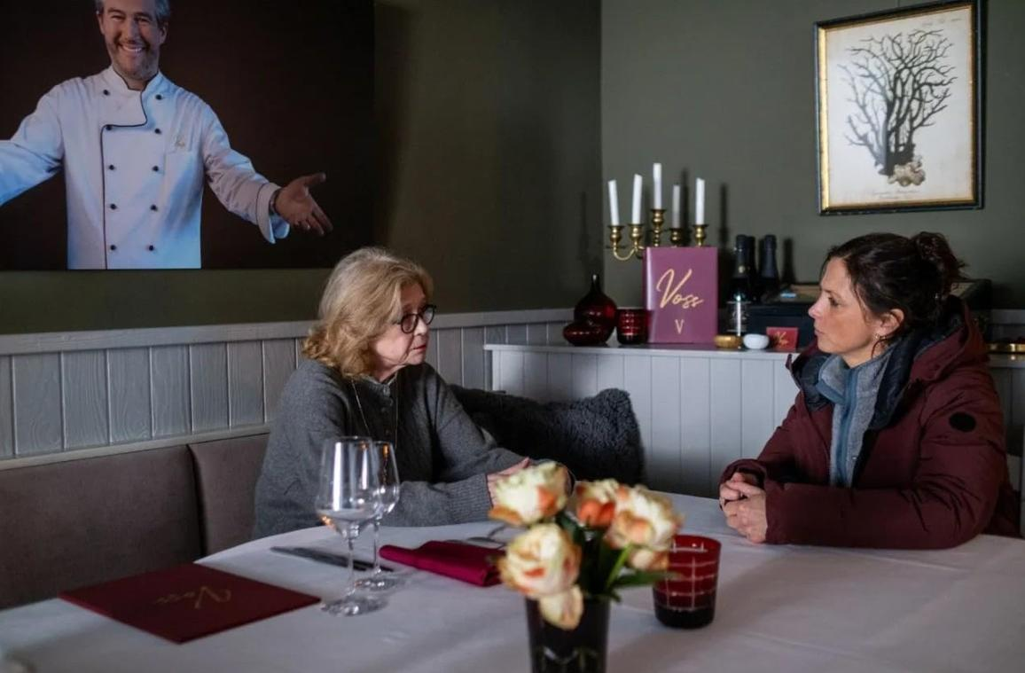 Zwei Frauen sitzen an einem Tisch in einem Restaurant. Ein Kochbild hängt an der Wand.
