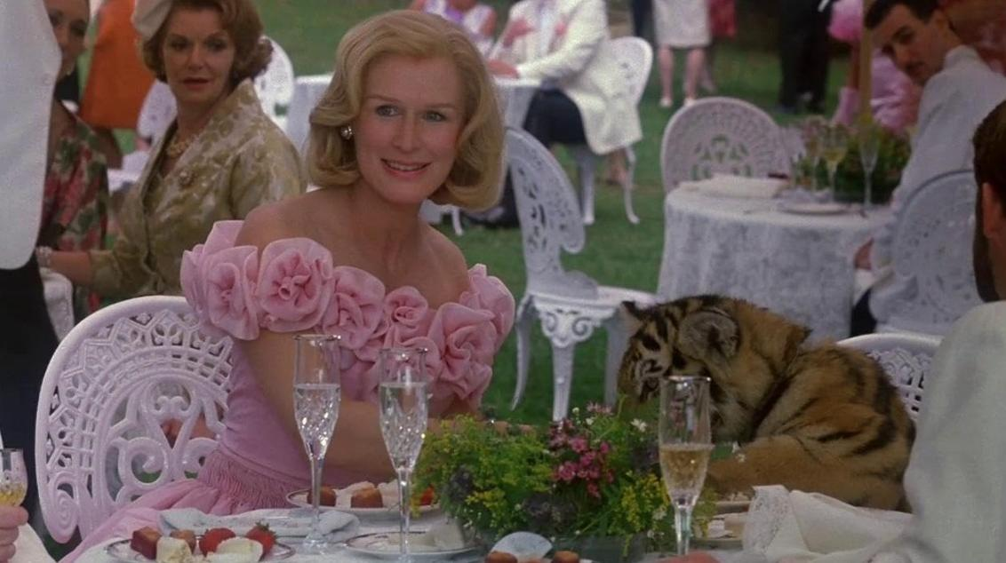 Eine Frau in rosa Kleid sitzt am Tisch mit einem Tiger, der daneben liegt.