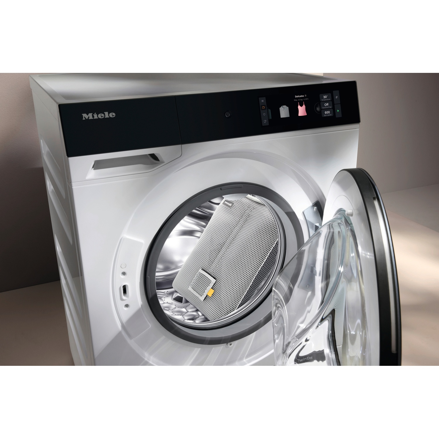 Machine à laver Miele blanche porte ouverte avec un panier à linge dans le tambour.