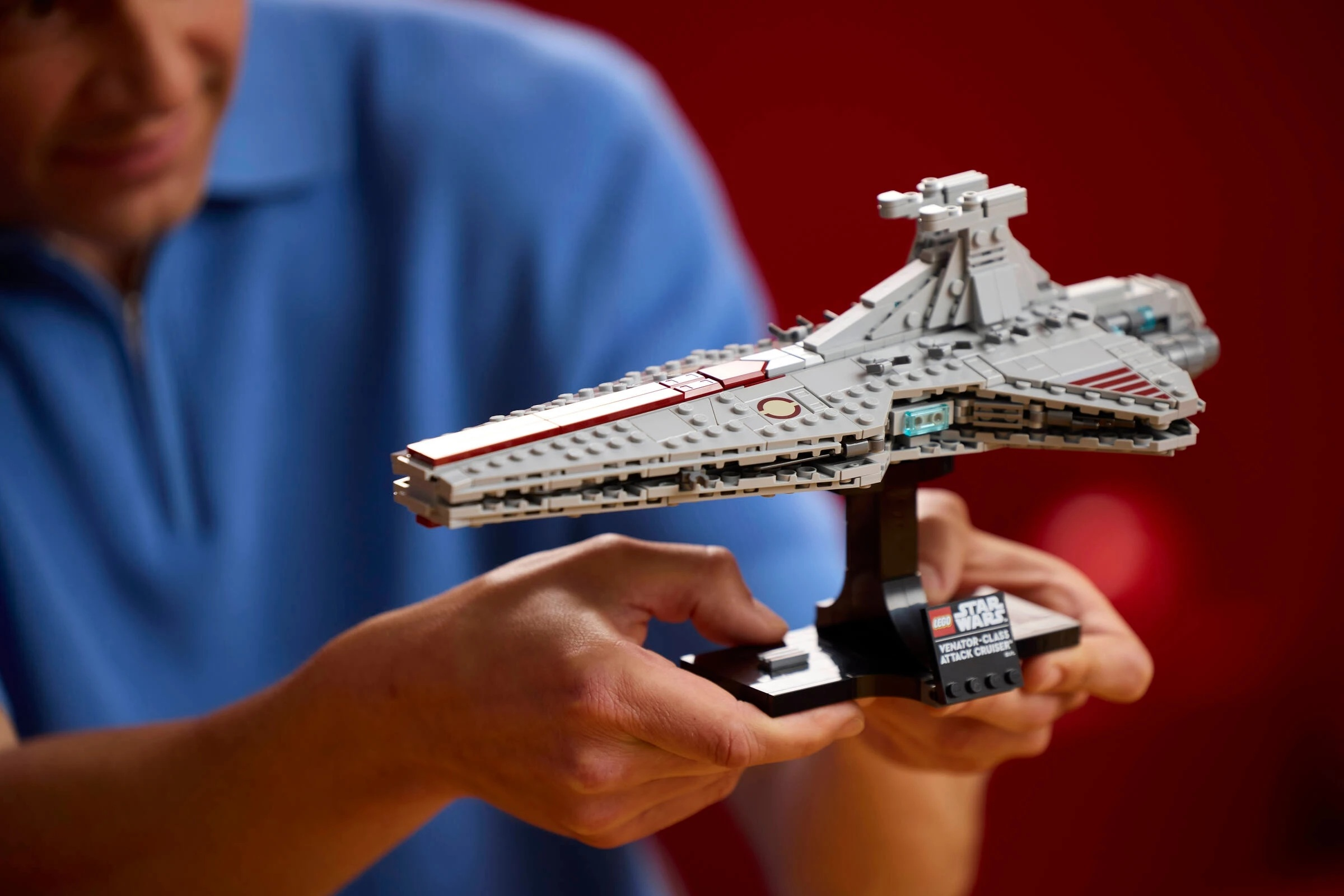 Mężczyzna w niebieskiej koszuli trzyma szary statek kosmiczny Lego klasy Venator.