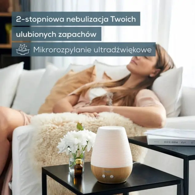 Kobieta relaksuje się na sofie obok dyfuzora i kwiatów.