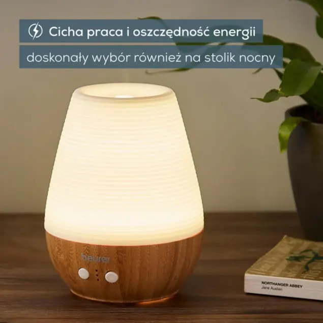 Podświetlony dyfuzor z drewnianą podstawą stoi obok książki i rośliny.