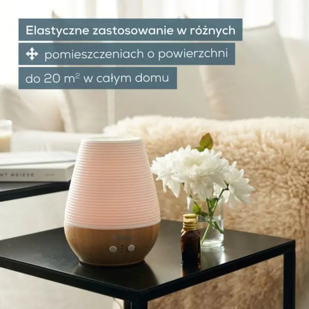 Dyfuzor z drewnianą podstawą stoi na czarnym stole obok kwiatów.