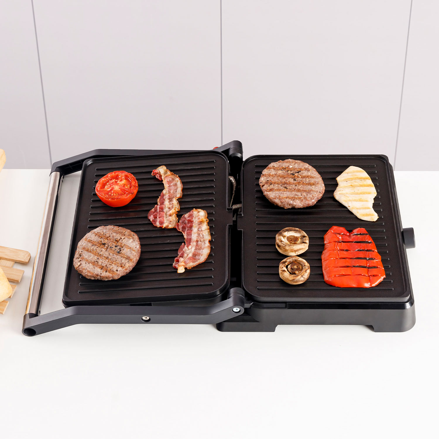 Una parrilla eléctrica con hamburguesas, tocino, champiñones, tomate, pimiento y pollo.