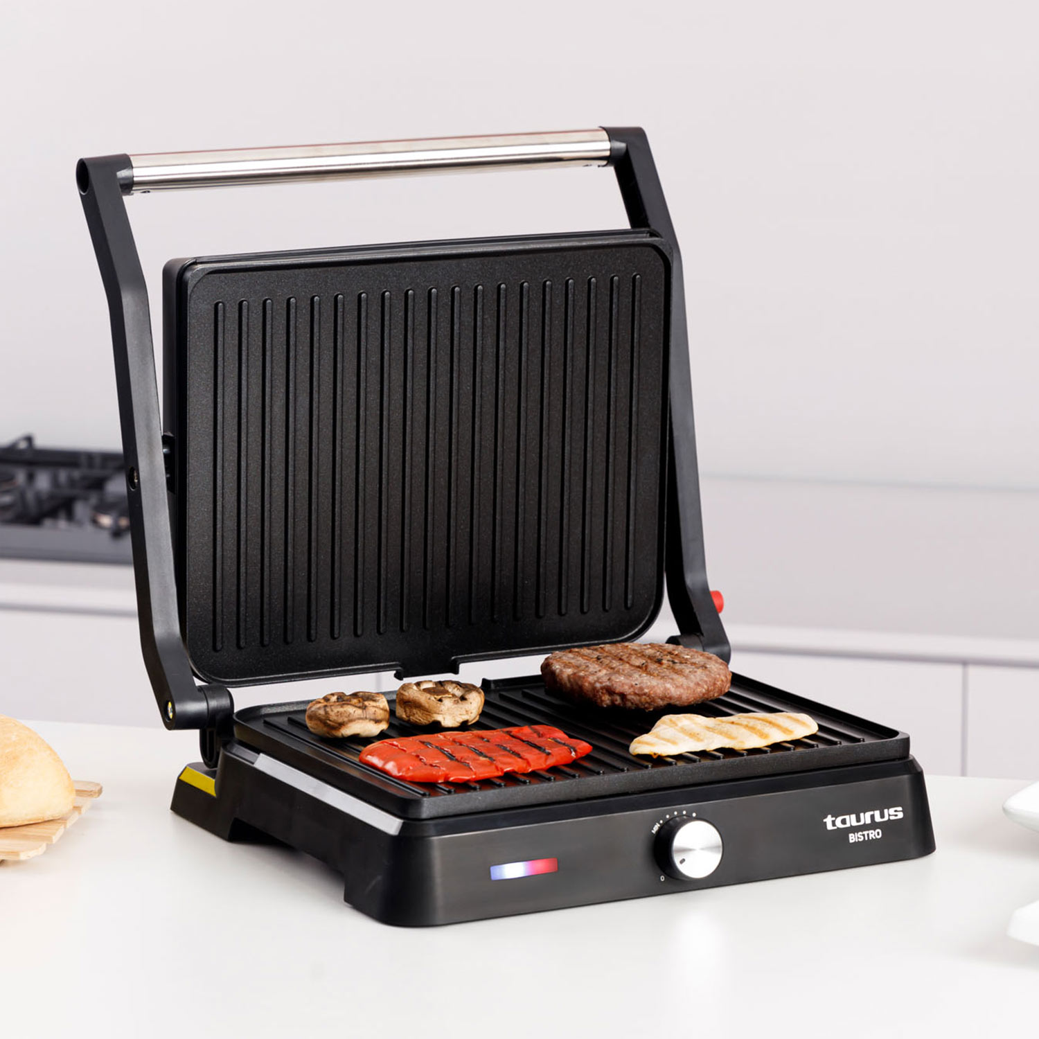 Una parrilla de contacto negra abierta cocinando hamburguesa, pollo, champiñones y pimientos.