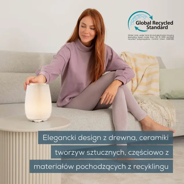 Kobieta siedzi na sofie, obsługując dyfuzor. Widoczna jest etykieta certyfikatu.
