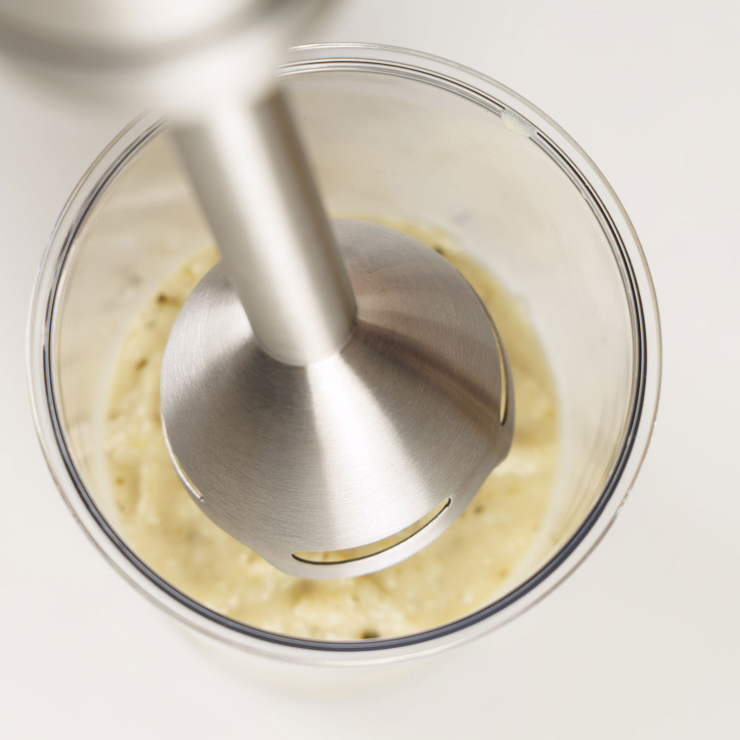 La cabeza de una batidora de mano en un vaso con puré amarillo.