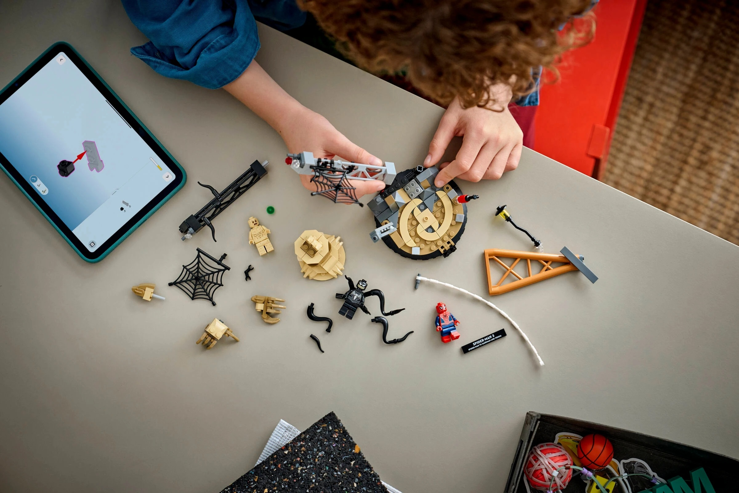 Dziecko buduje klocki Lego z instrukcją na tablecie. Figurki i części Lego na stole.