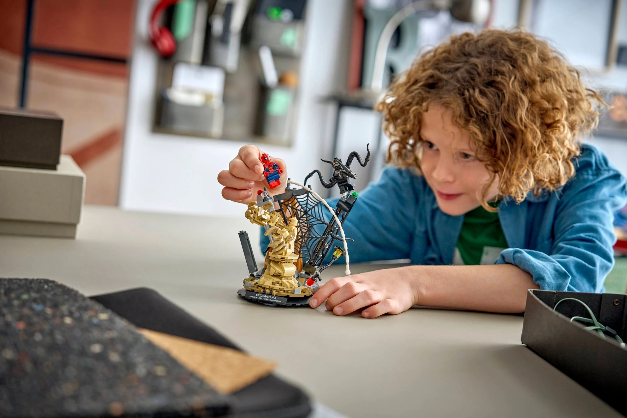 Chłopiec bawi się figurkami Lego Spider-Mana, Sandmana i Venoma na stole.