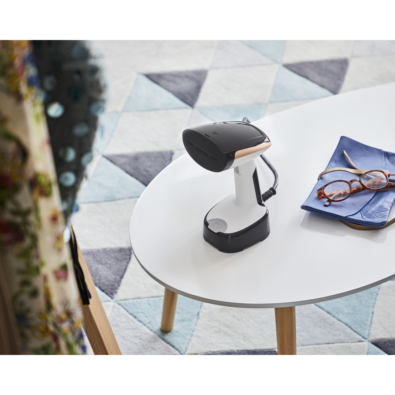 Un vaporizzatore portatile su un tavolo bianco accanto a occhiali e una pochette blu.