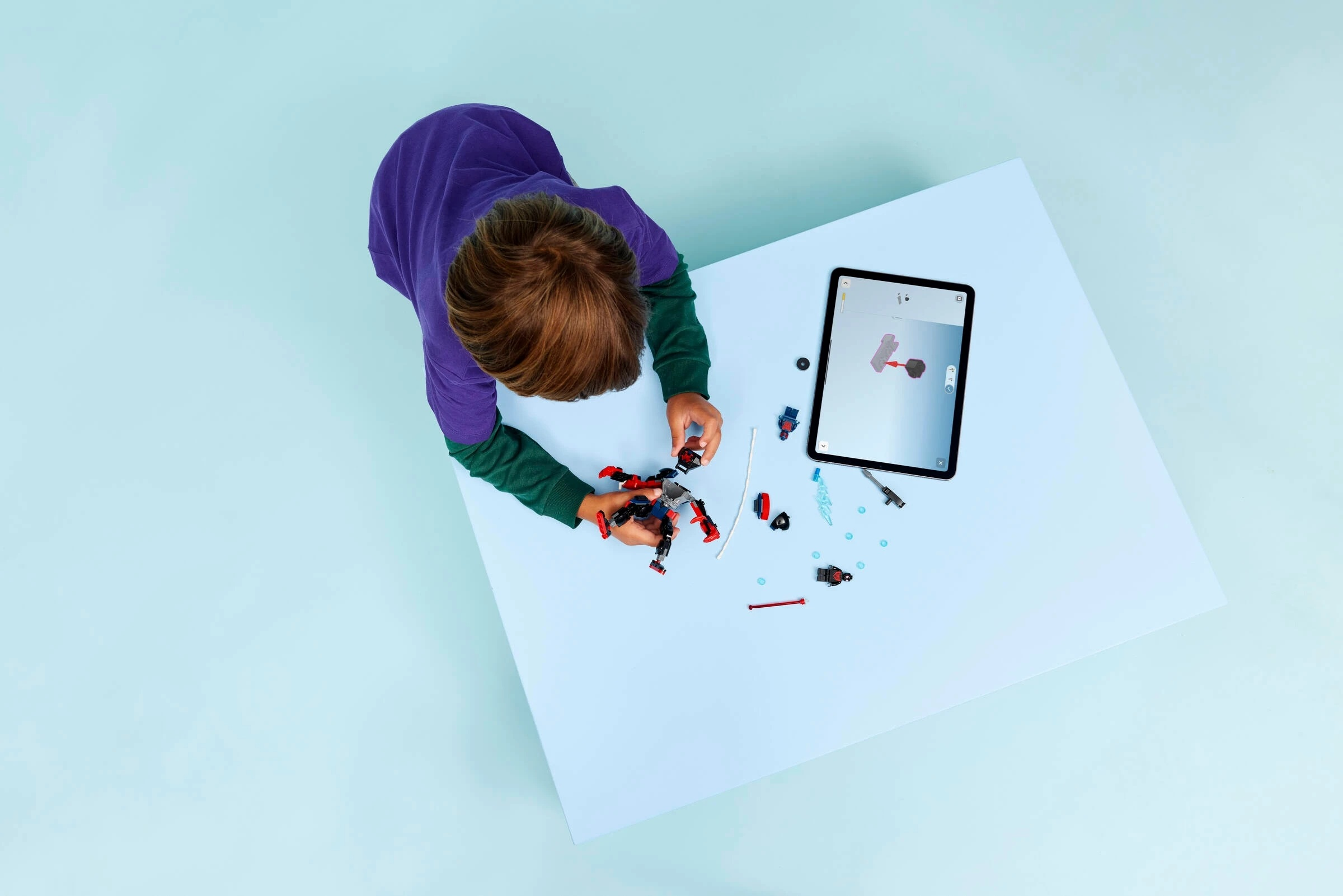 Dziecko buduje robota z czerwonych i niebieskich części, z instrukcjami na tablecie.