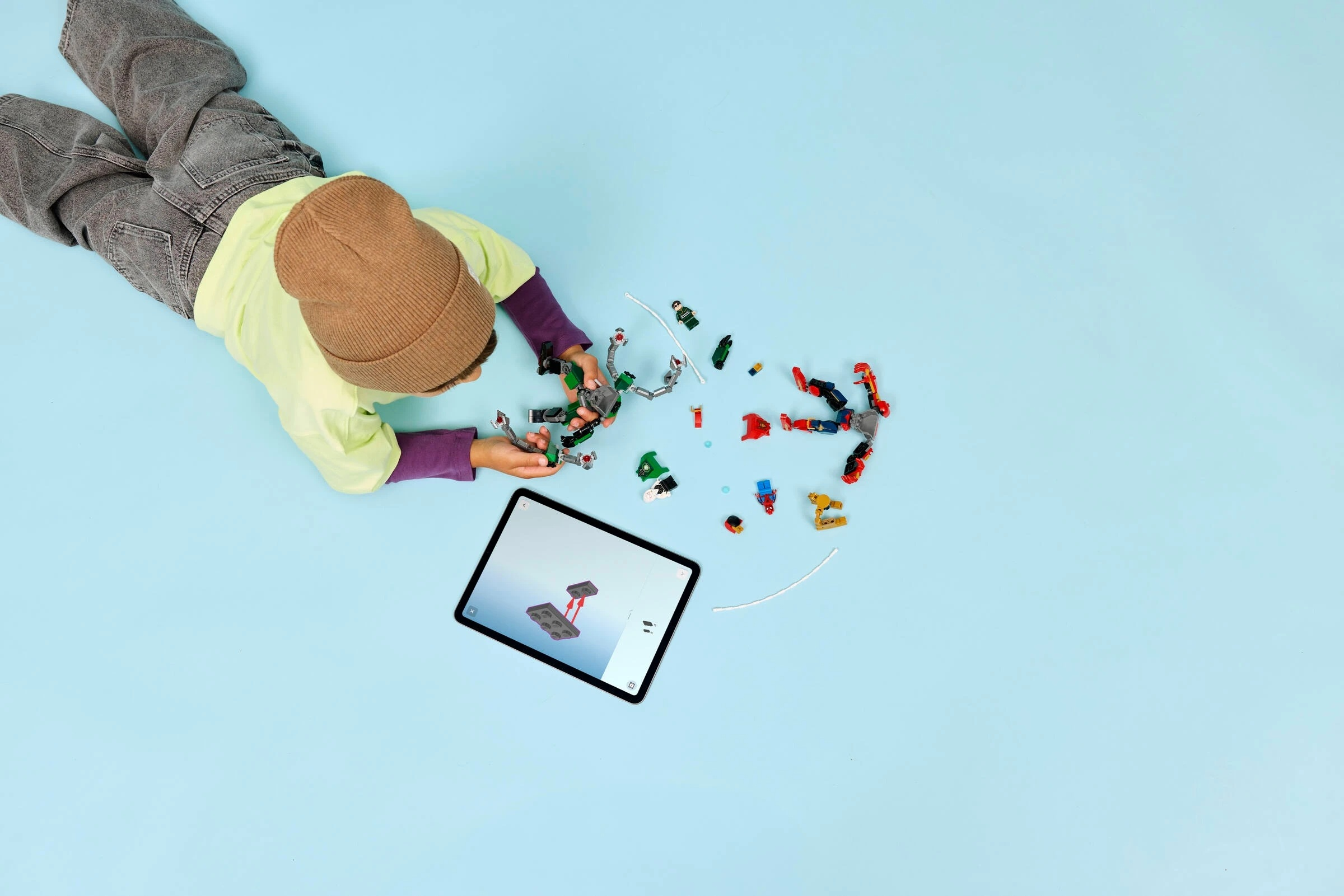 Dziecko buduje Lego z instrukcją na tablecie. Kolorowe klocki leżą na niebieskiej powierzchni.