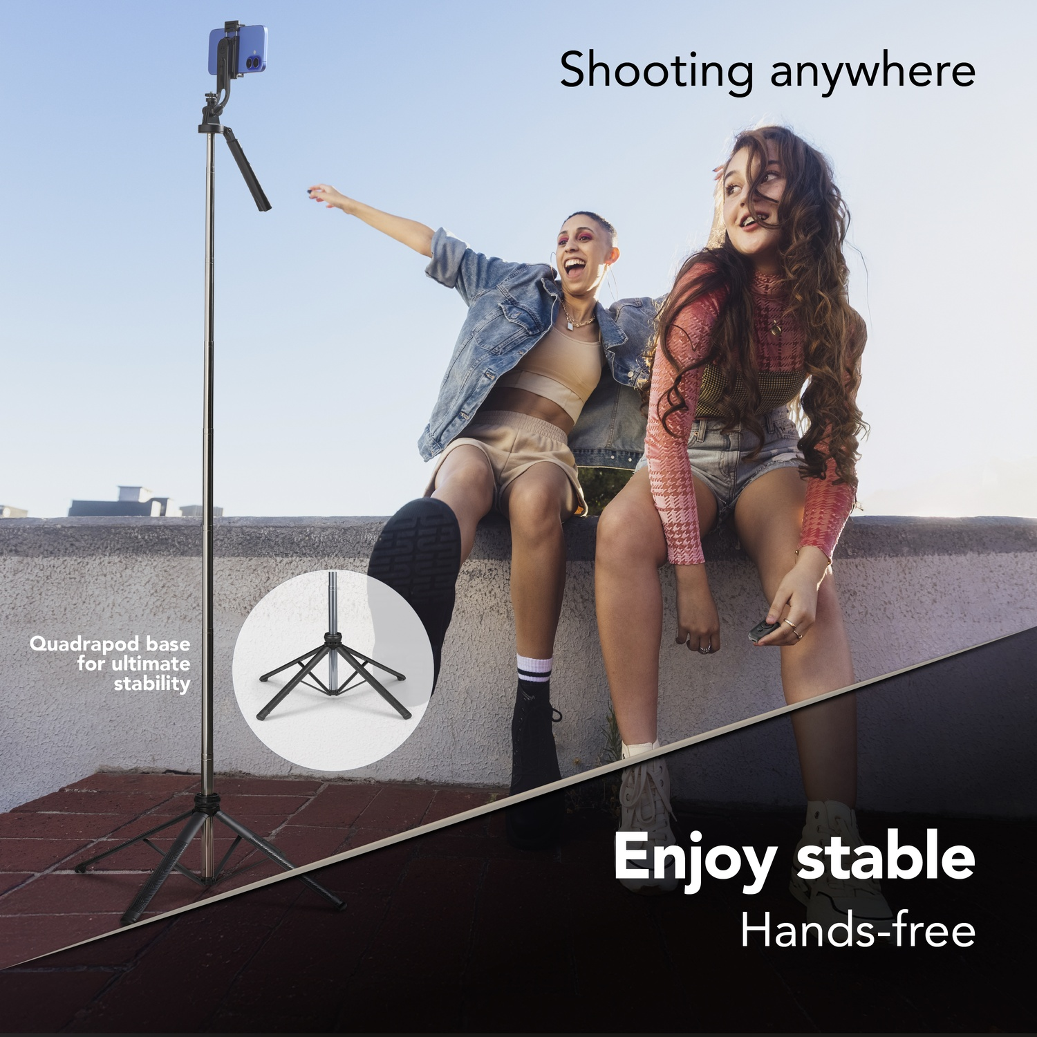 Due donne sedute su un muro, un selfie stick con telefono nelle vicinanze. Base quadpod.