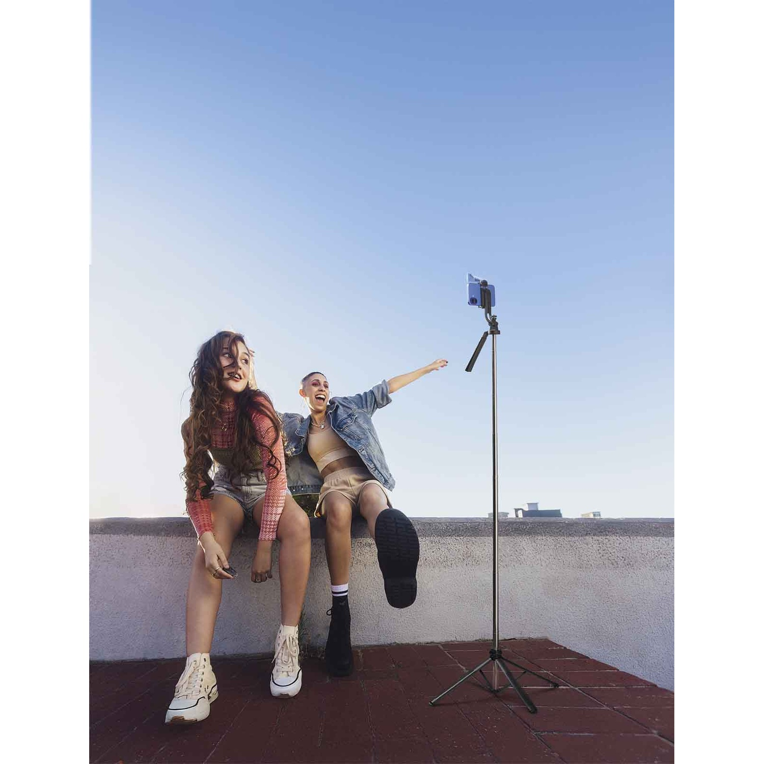 Due donne sedute su un muro, una filma con un telefono su un treppiede.