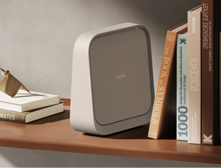 Szare urządzenie XGIMI stoi na półce obok książek i drewnianego ptaka.
