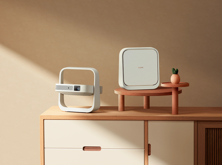 Biały projektor i urządzenie na drewnianej szafce przed brązową ścianą.