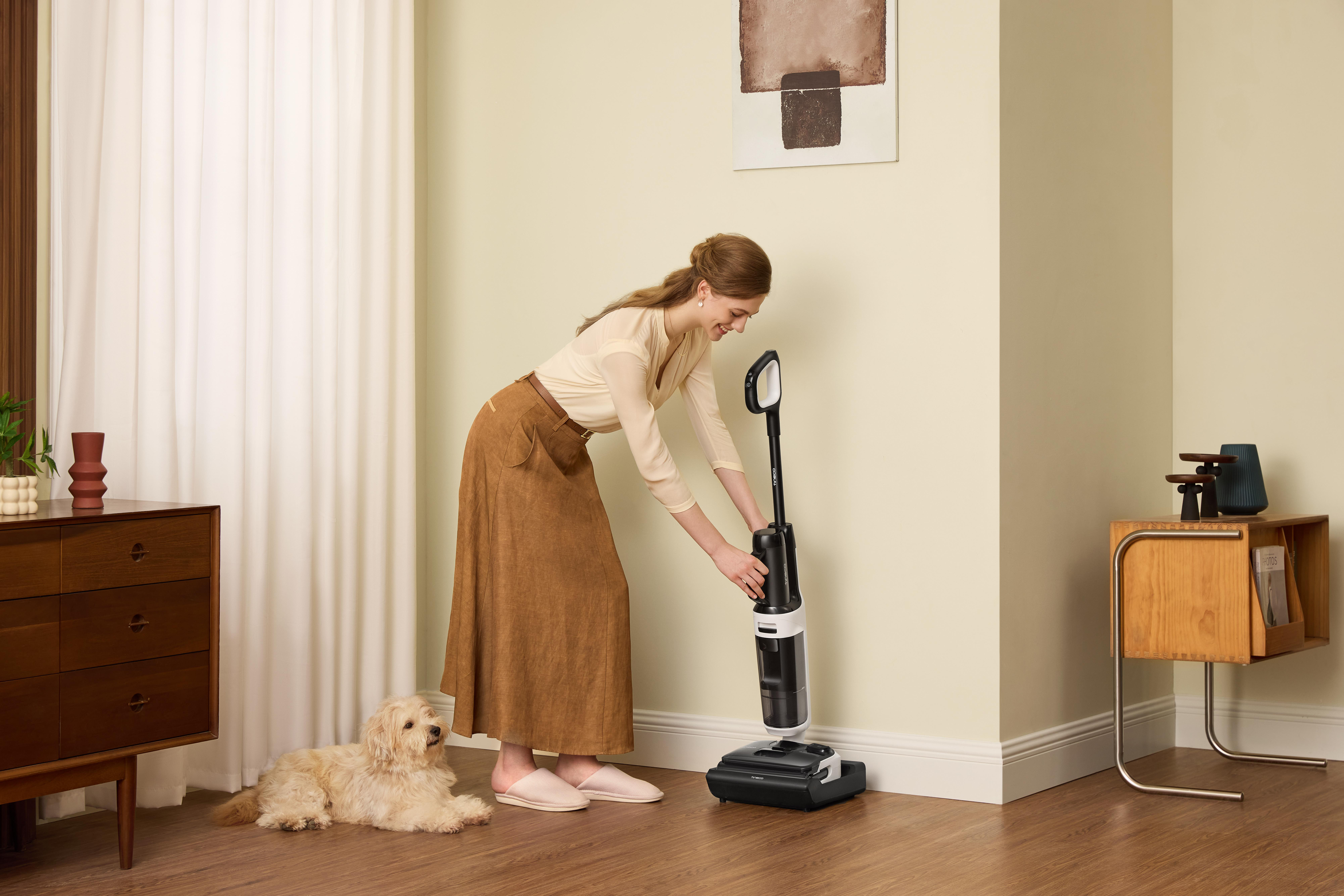 Frau mit Staubsauger und Hund in einem hellen Raum.
