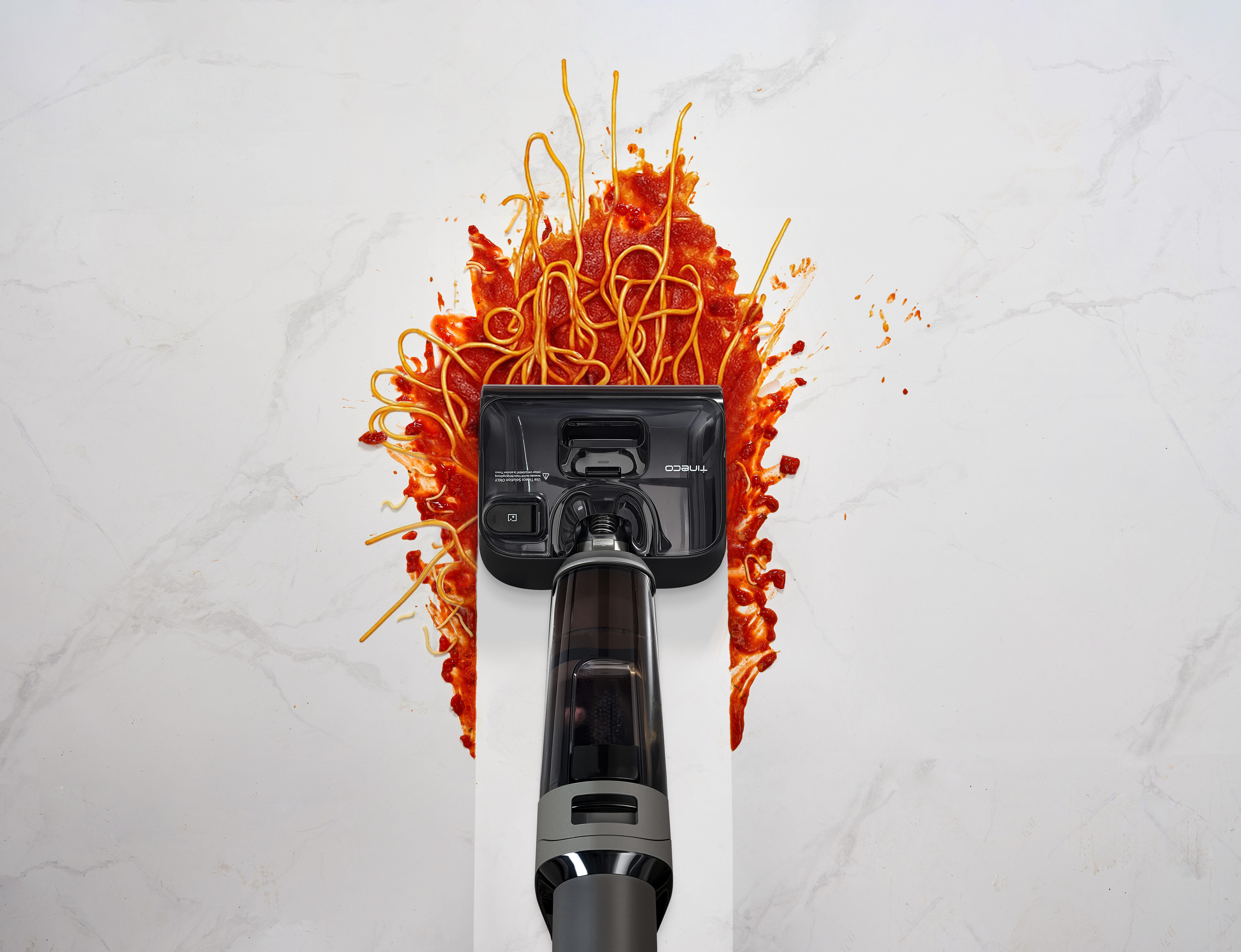 Ein schwarzer Staubsaugerreiniger saugt Spaghetti mit Tomatensoße auf.