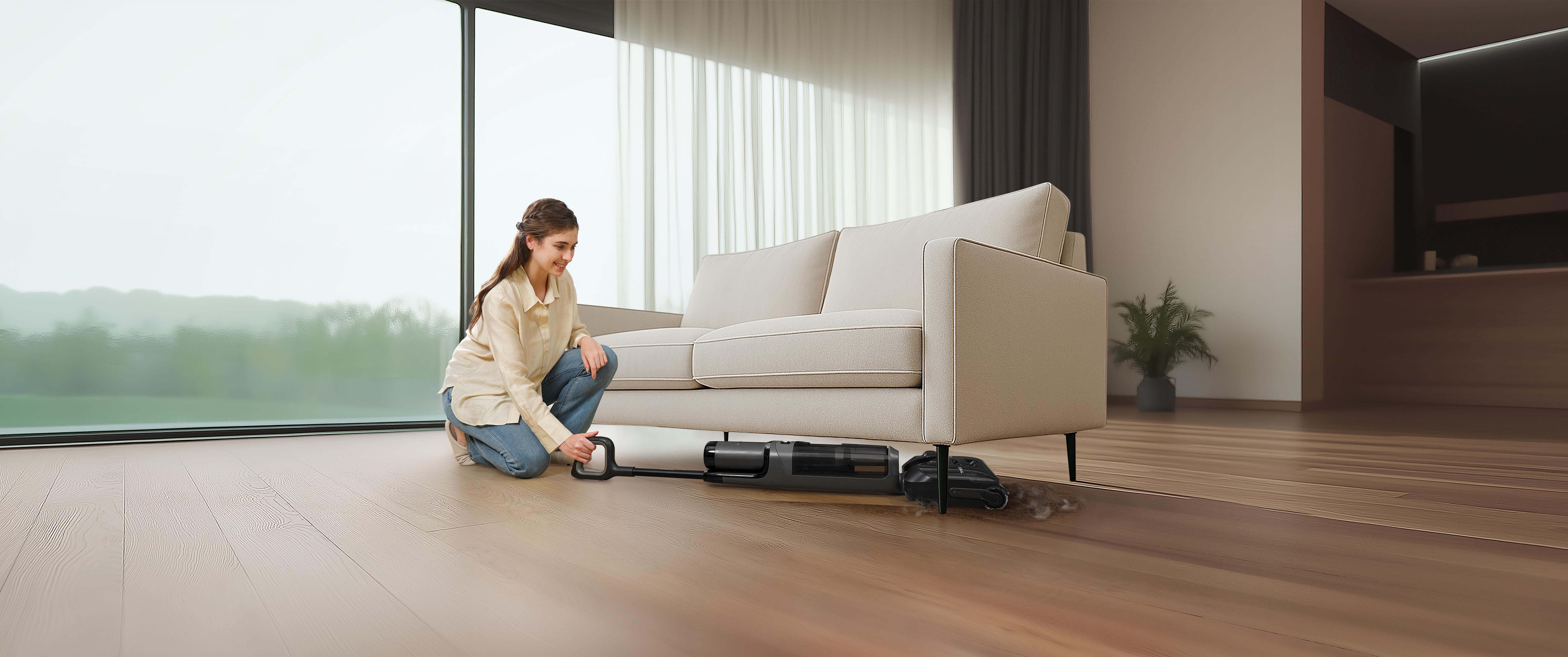 Eine Frau reinigt den Boden unter einem Sofa mit einem Nass-/Trockensauger.