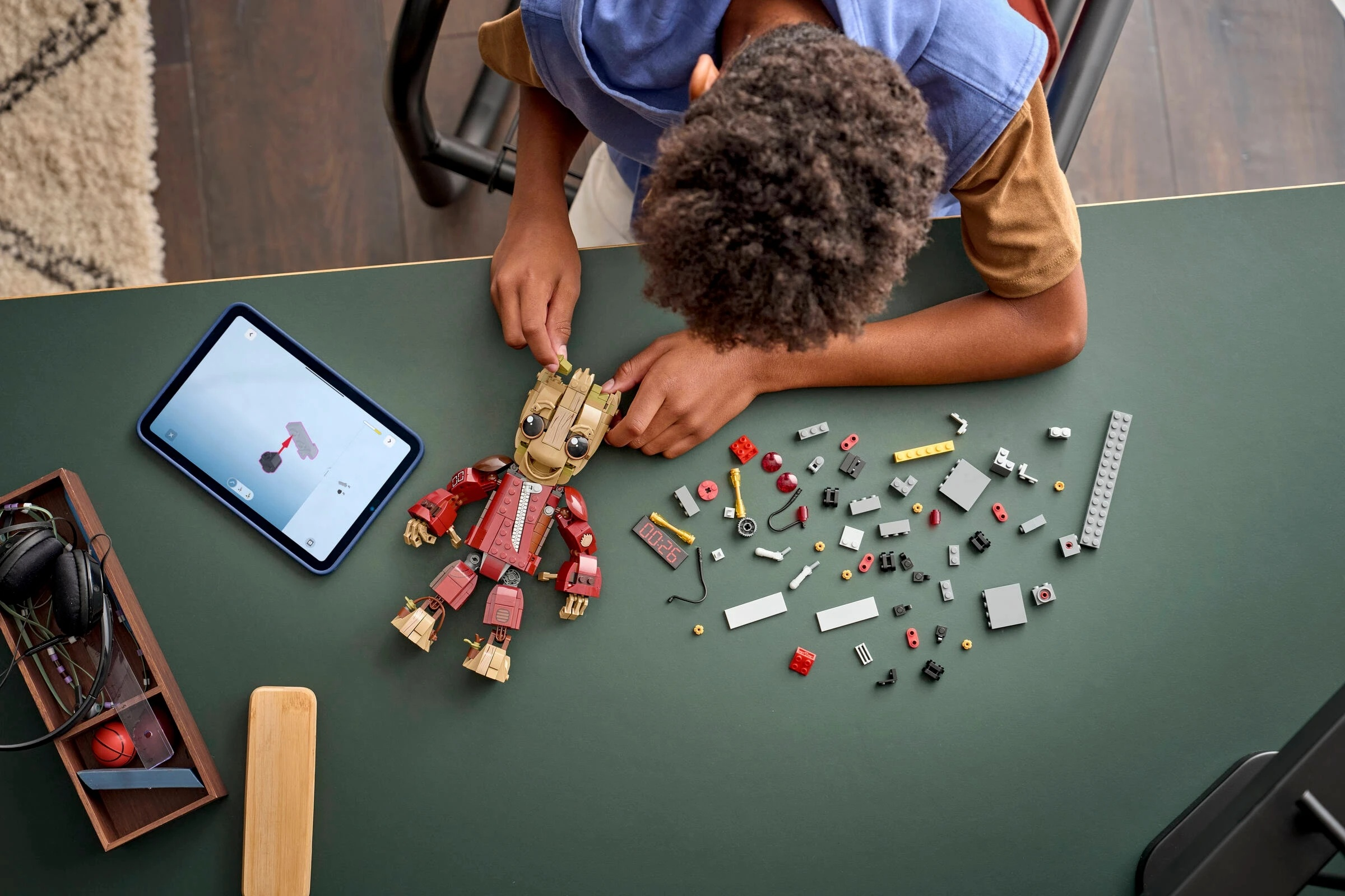 Dziecko buduje czerwoną figurkę Lego obok tabletu z instrukcjami budowania.