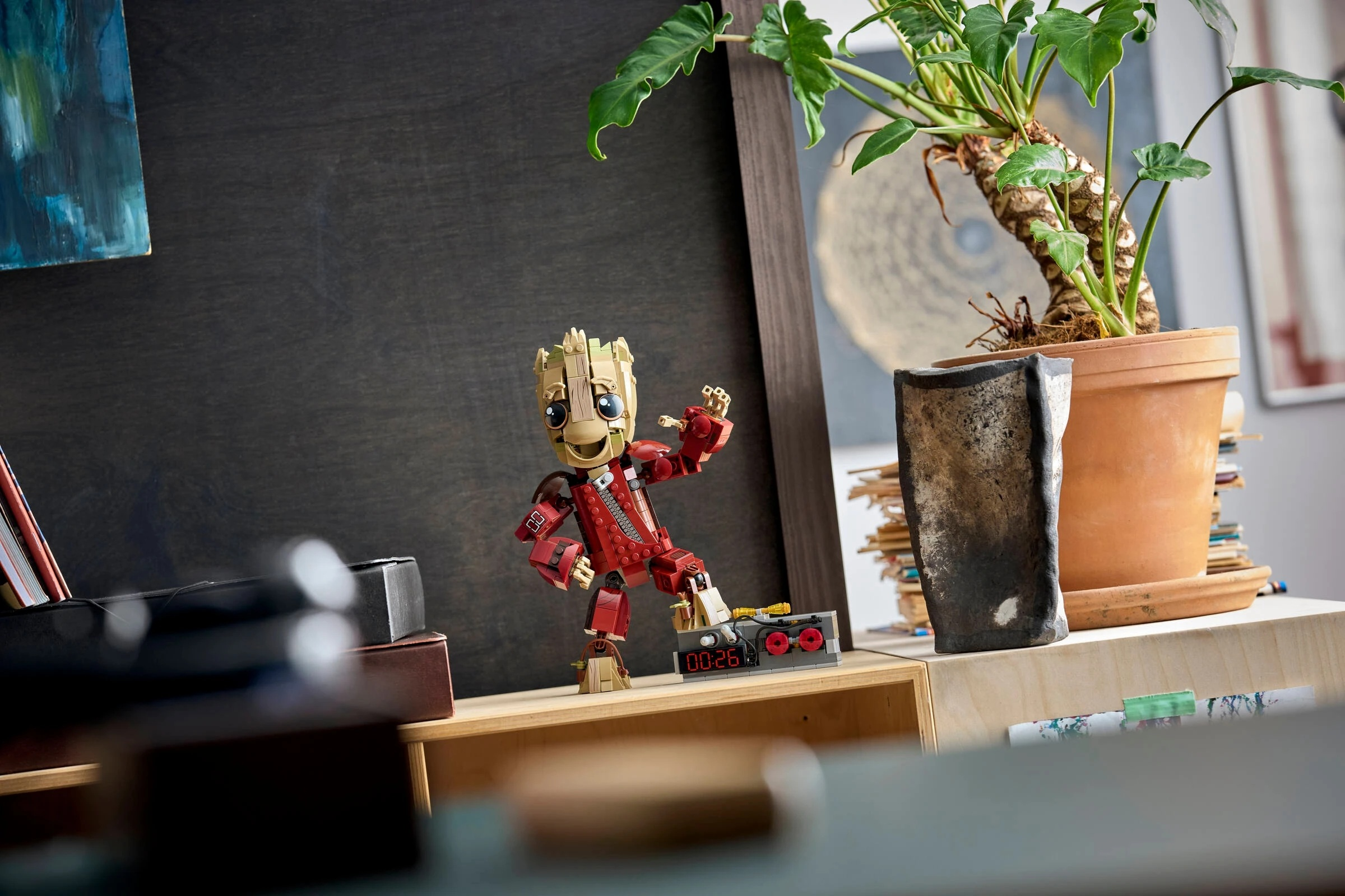 Figurka Lego Groot stoi na półce obok rośliny doniczkowej i budzika.