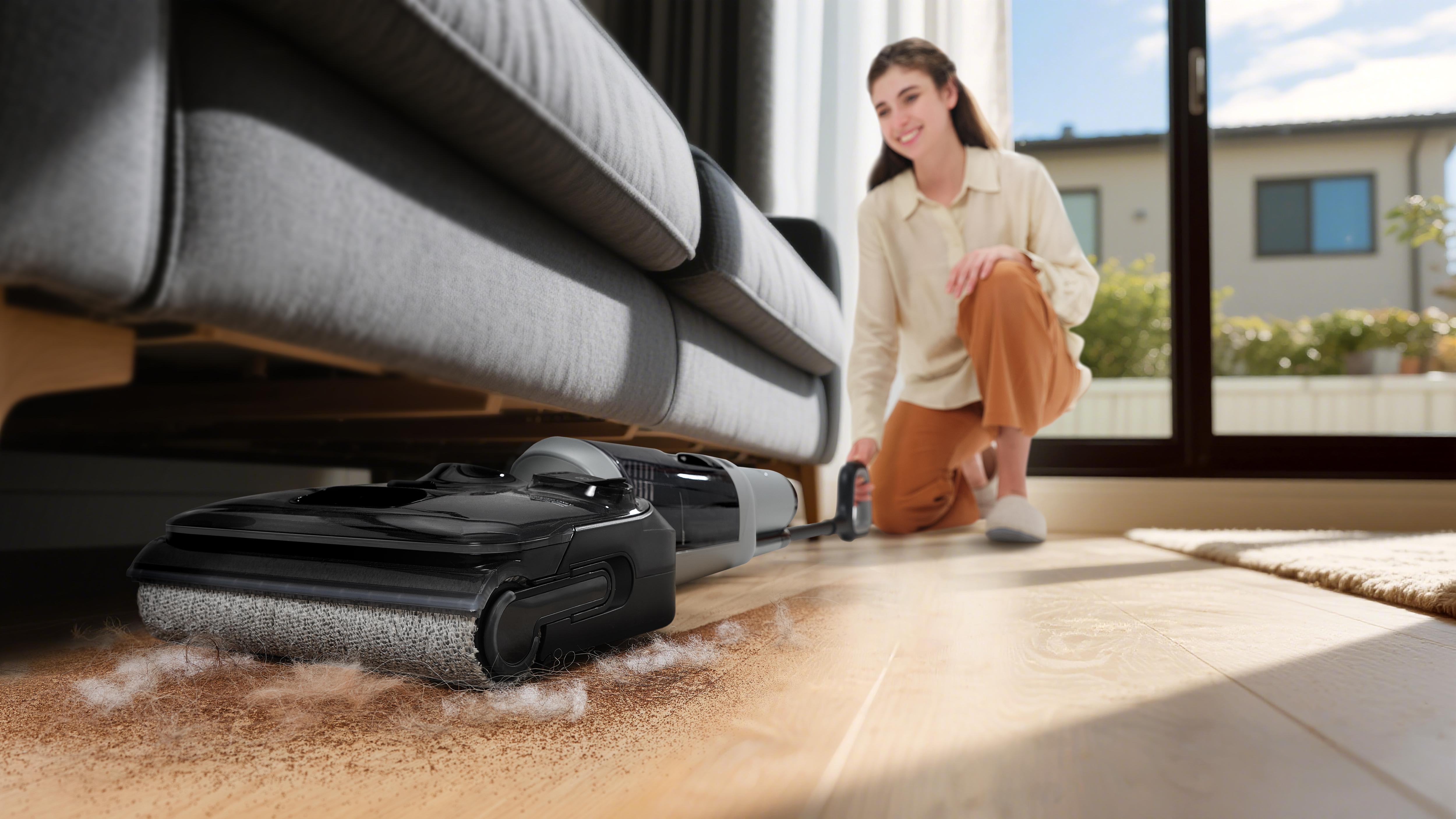 Eine Frau reinigt den Boden mit einem Staubsauger unter einem Sofa.