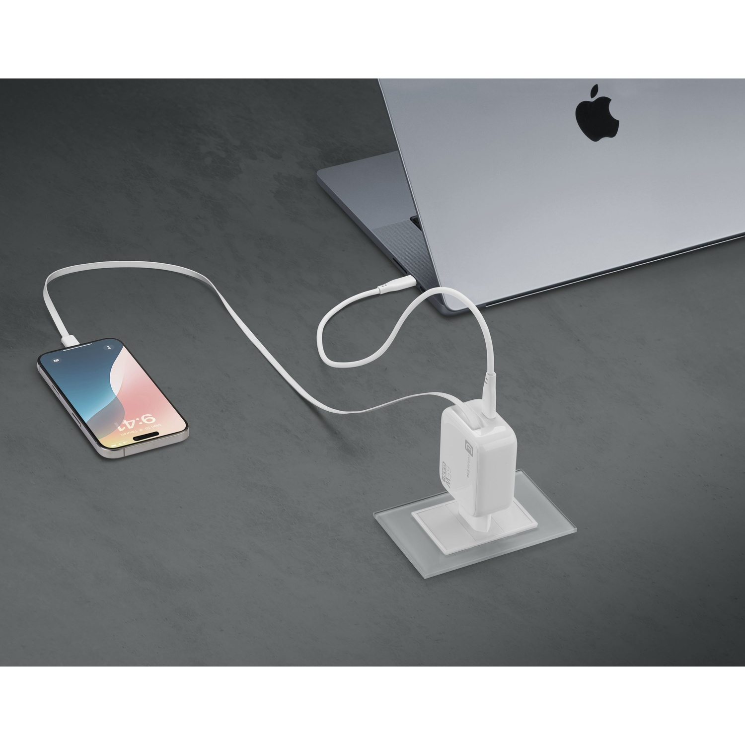 Un caricabatterie bianco collega un iPhone a un MacBook su un tavolo grigio.