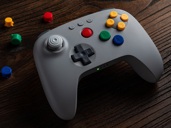 Grauer Controller mit bunten Knöpfen und Joystick auf Holztisch.