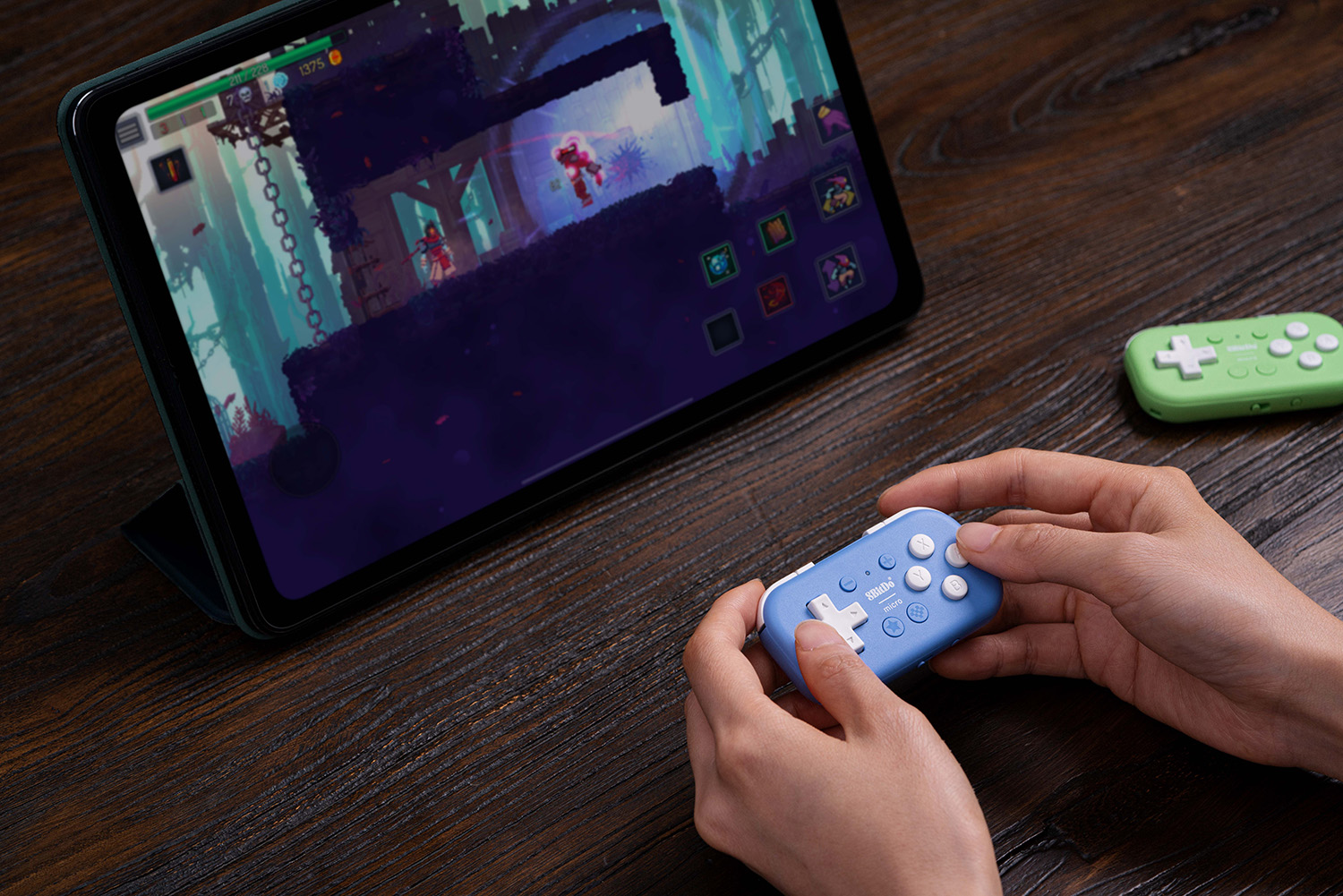 Hände halten blaue und grüne Controller vor einem Tablet mit einem Spiel.