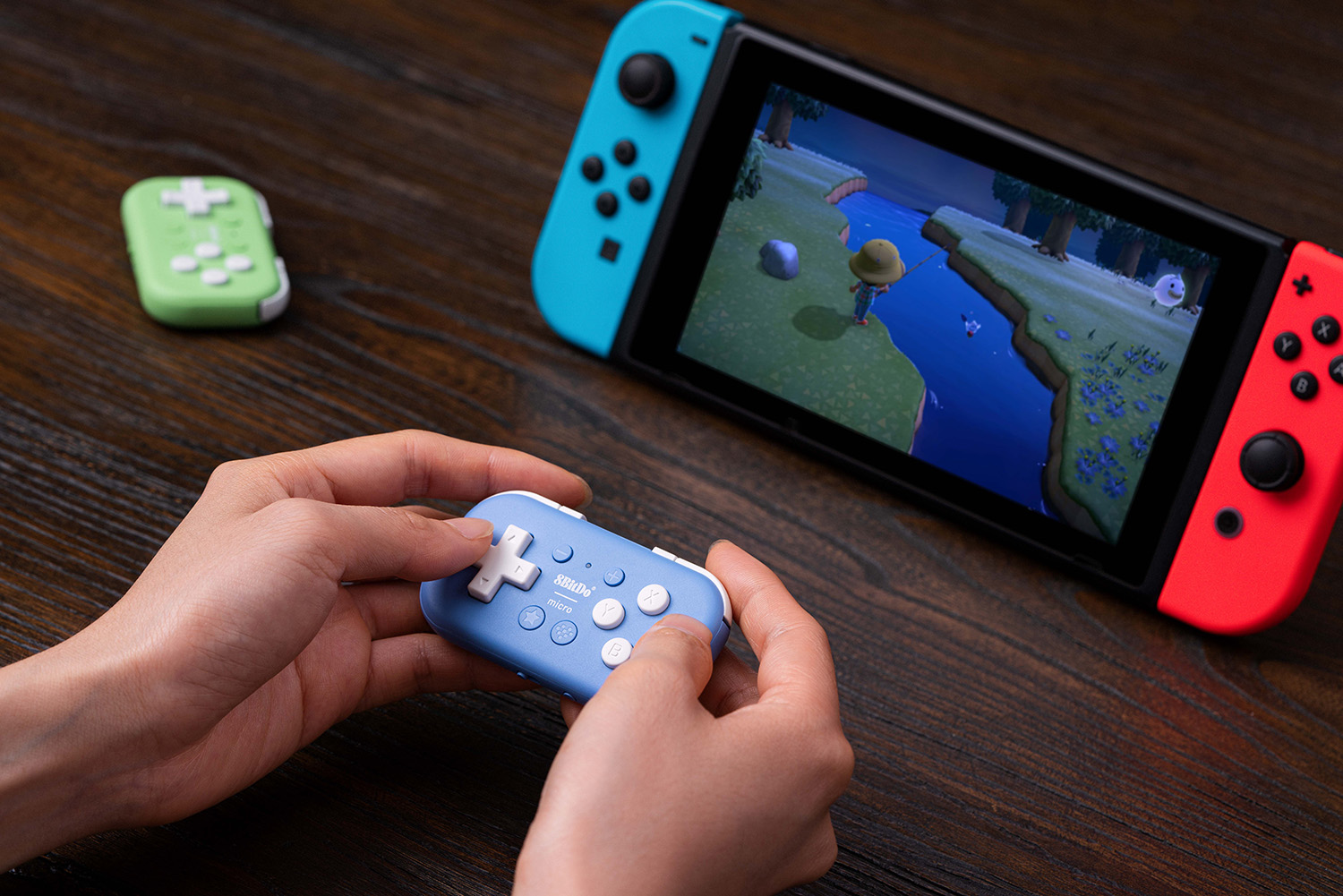 Person hält einen blauen Controller. Nintendo Switch spielt Spiel. Grüner Controller liegt daneben.