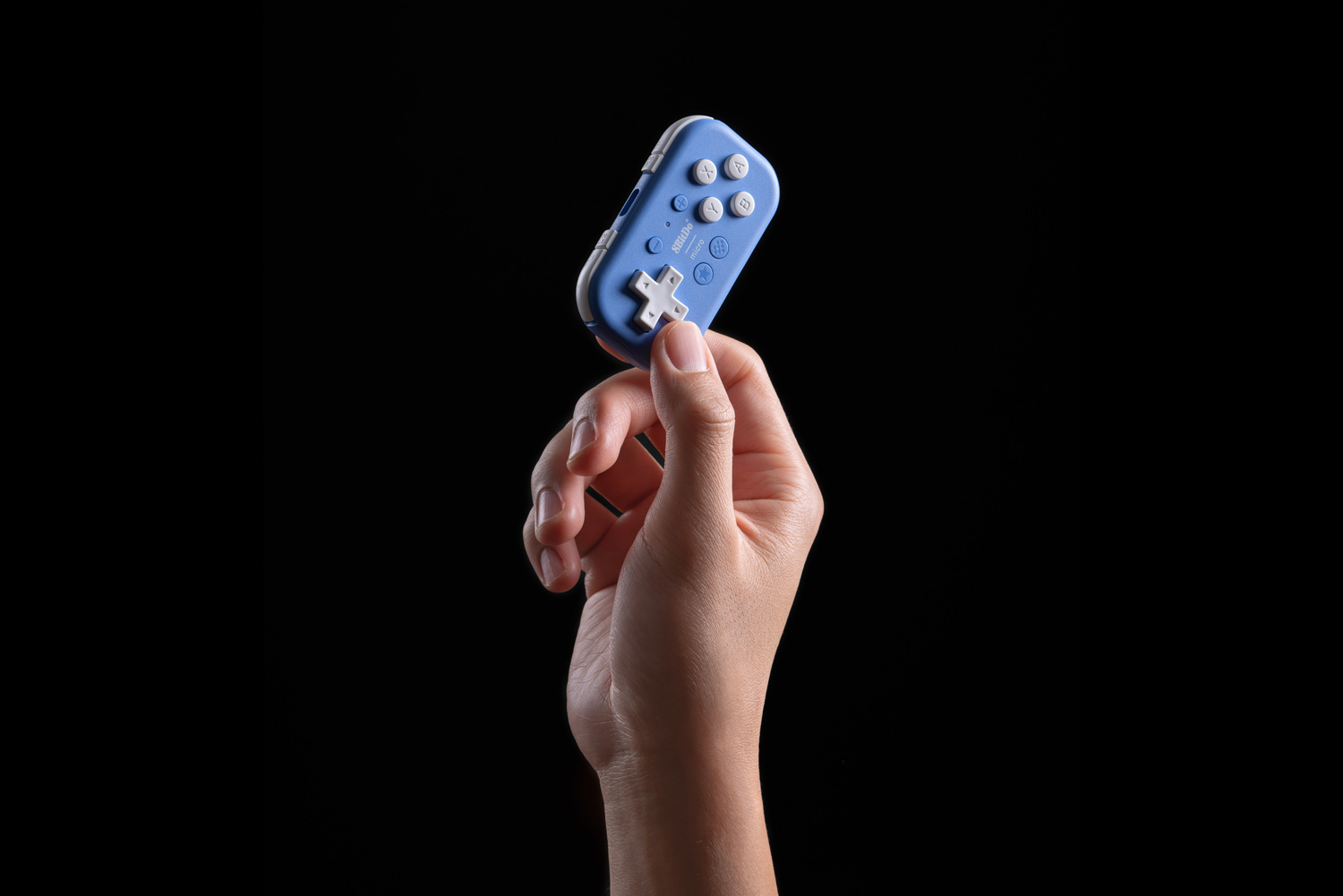 Eine Hand hält einen kleinen blauen Gamecontroller mit weißen Knöpfen.