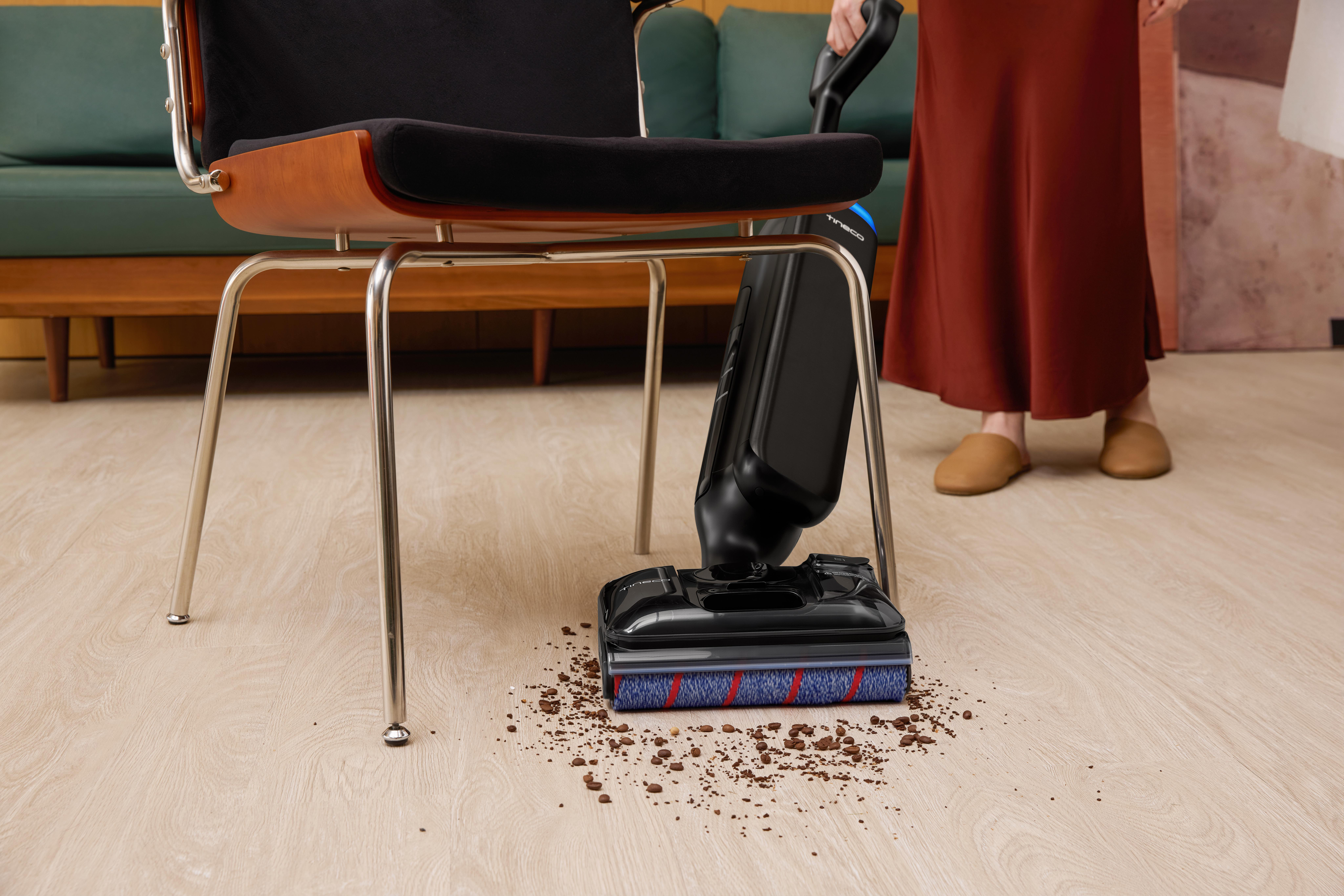 Ein schwarzer Bodenreiniger reinigt Kaffeebohnen auf einem Holzboden unter einem Stuhl.