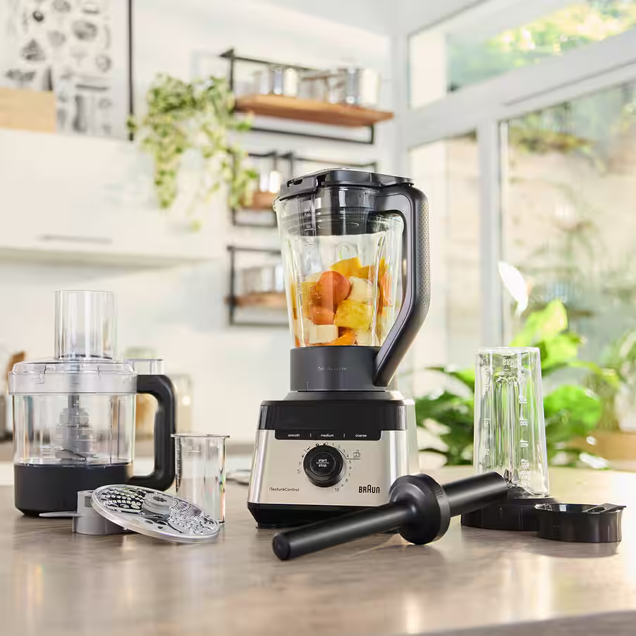 Ein Küchenmixer und ein Food Processor mit Obst im Mixbehälter stehen auf einer Arbeitsplatte.