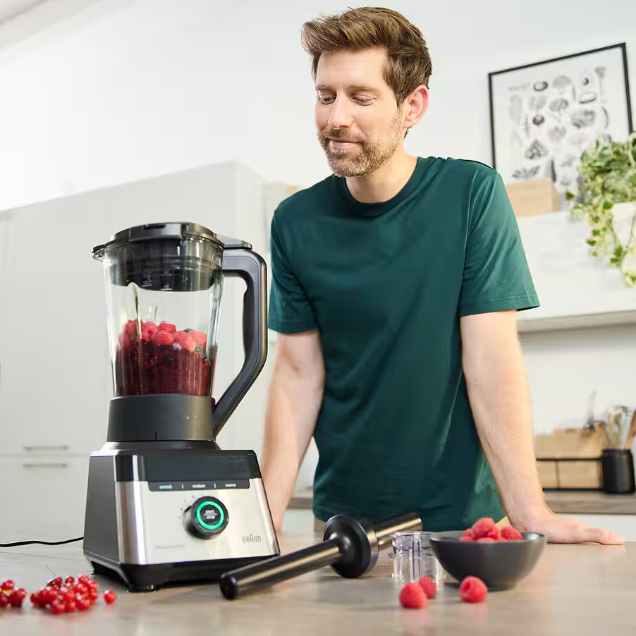 Mann in dunkelgrünem Shirt mit Mixer voller Beeren und rotem Johannisbeer-Fruchtmix.
