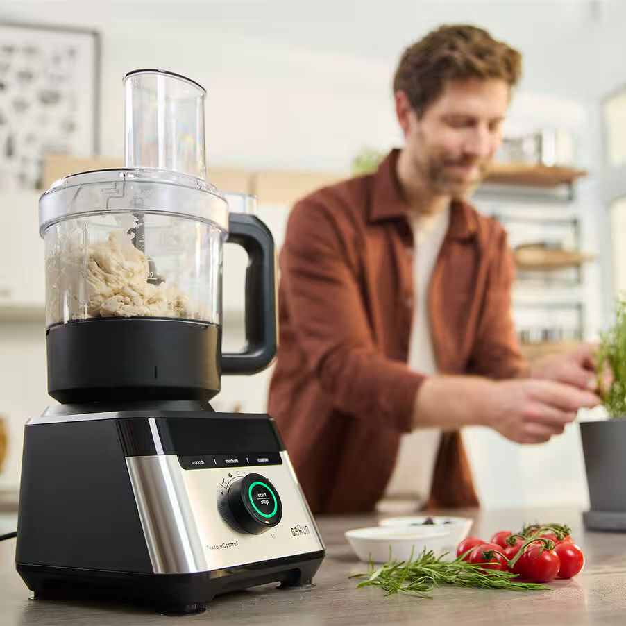 Küchenmaschine mit Teig im Behälter, Mann im Hintergrund pflanzt eine Pflanze.