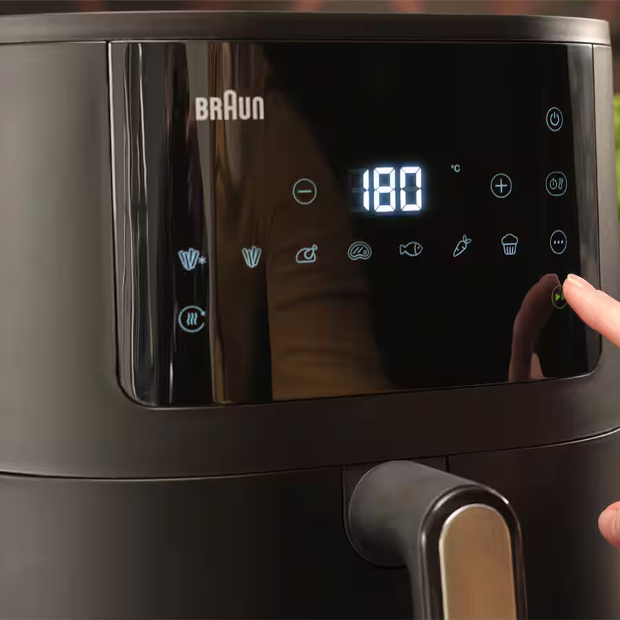 Un doigt appuie sur le bouton de démarrage d'un panneau de commande de friteuse à air Braun noir.