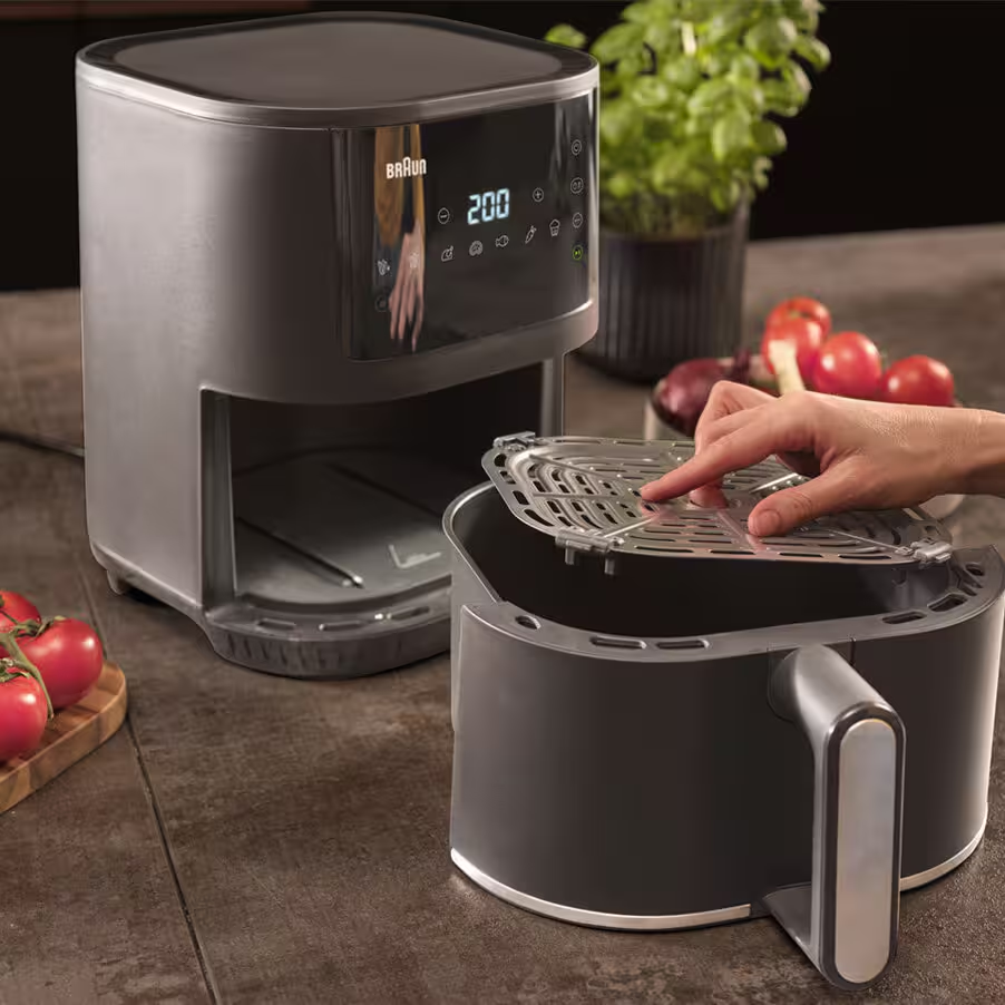 Une friteuse à air Braun noire avec écran numérique. Un panier est inséré.