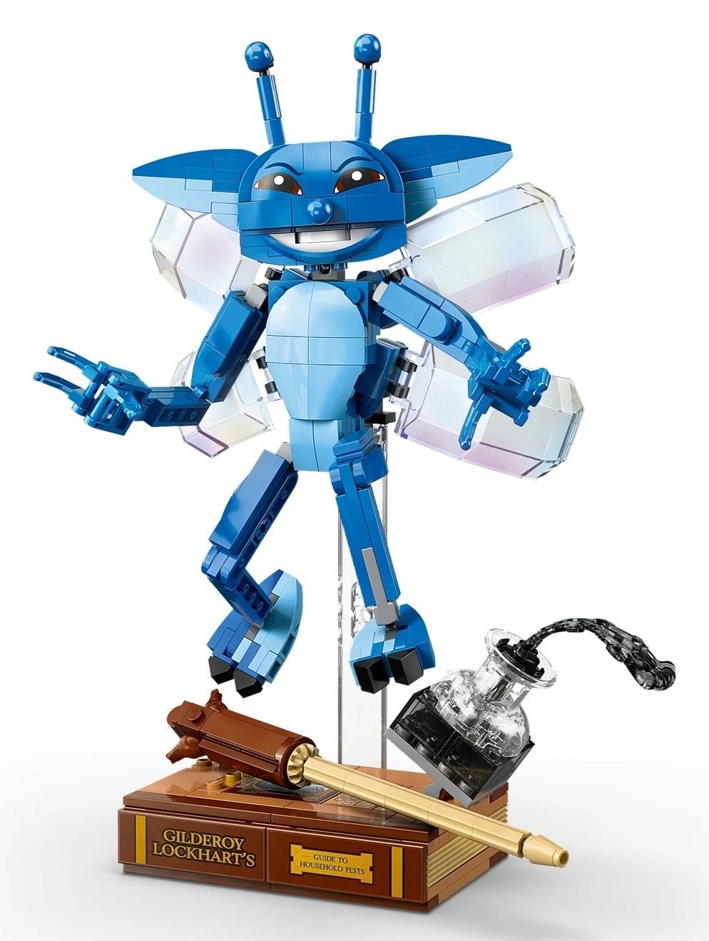 Niebieski stworek Lego stoi na książce obok kałamarza i różdżki.
