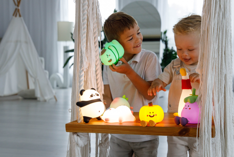 Dwóch chłopców z uroczymi lampkami nocnymi na półce-huśtawce w jasnym pokoju.