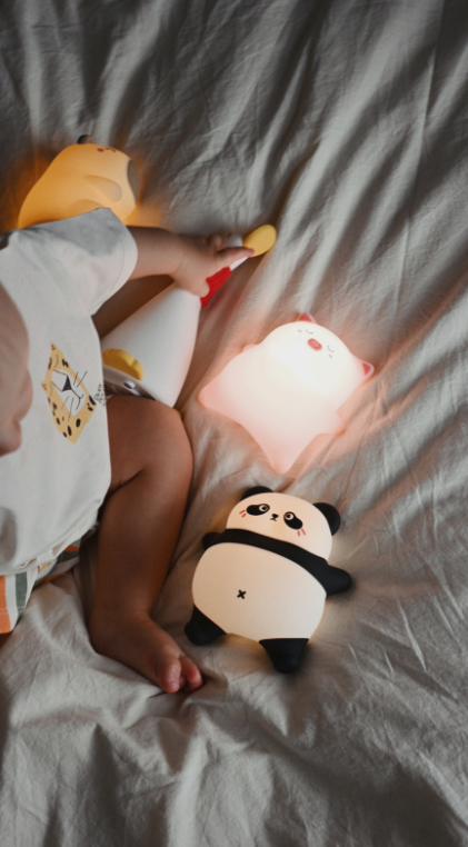 Niemowlę leży na łóżku, bawiąc się trzema małymi lampkami nocnymi.