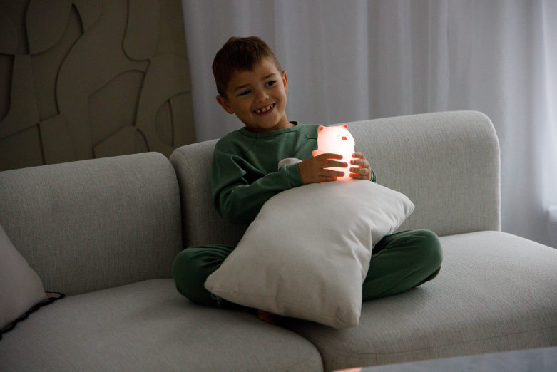 Chłopiec siedzi na sofie, trzymając świecącą lampkę w kształcie misia.