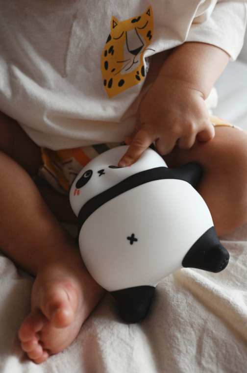 Niemowlę trzyma lampkę-pandę; niemowlę nosi koszulkę z nadrukiem pantery.