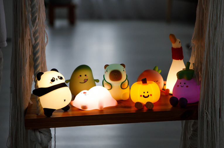 Urocze lampki nocne w kształcie zwierząt i warzyw na drewnianej półce.