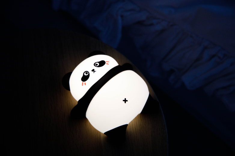 Świecąca lampka nocna panda na stoliku nocnym obok łóżka.