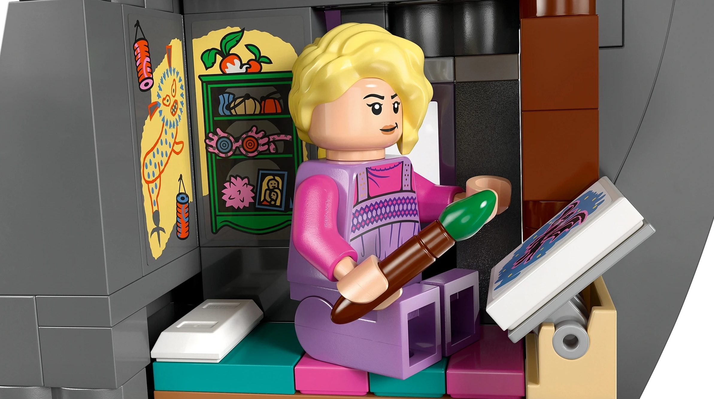 Figurka Lego z blond włosami maluje obraz na sztalugach.